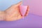 Pink reusable menstrual cup in female hand on color background. Woman critical days, gynecological menstruation cycle.