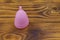 Pink reusable silicone menstrual cup on wooden background. Concept of feminine hygiene, gynecology and health