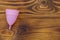 Pink reusable silicone menstrual cup on wooden background. Top view, copy space. Concept of feminine hygiene, gynecology