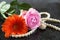 A pink rose and an orangery gerbera lie on a dark granite surface in the rain, alongside pearl beads and an earring