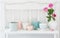 Pink roses in vase and dinnerware on white wooden shelf