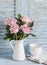 Pink roses in a white enameled pitcher and ceramic white bowls on blue wooden rustic background. Kitchen still life