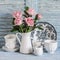 Pink roses in a white enameled pitcher, vintage crockery on blue wooden rustic background. Kitchen still life in vintage style.