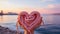 A pink sailor\\\'s rope rolled into a heart shape held by female hands by the sea. Heart-shaped sailor knots.