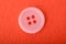 Pink sewing button isolated on a red background