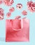 Pink shopping bag with flying flowers at pastel blue wall background. Branding mock up. Copy space. Creative summer concept