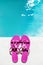 Pink slippers near swimming pool at poolside. Summer vacation. Pink sandals by swimming pool. Blue sea surface with waves, texture