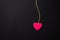 Pink small heart on a string on a dark background.