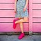 Pink sneakers on girl legs on the grunge wooden pink wall background. Street style. Girl wearing sneakers and summer skirt.
