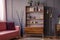 Pink sofa next to wooden cabinet and gold lamp in grey living room interior. Real photo