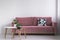 Pink sofa with a patterned pillow and two coffee tables with plants on a white wall in a living room interior. Real photo