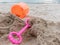 Pink spade and orange plastic bucket of sand tool toy set for kid and toddler on the sand over beach background