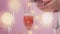 Pink sparkling wine with womans hand and glasses on pink background with christmas lights