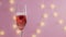 Pink sparkling wine with womans hand and glasses on pink background with christmas lights