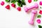 Pink sport dumbbells, and red roses on white wooden background,