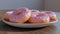 Pink sprinkled donuts on a plate with wooden backdrop.