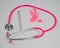 Pink stethophonendoscope, satin ribbon and scalpel on white background.