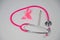 Pink stethophonendoscope, satin ribbon and scalpel on white background.