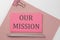 Pink sticker on pink paper with pencil on a white background with text OUR MISSION