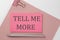 Pink sticker on pink paper with pencil on a white background with text TELL ME MORE