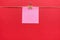 Pink sticky note hanging on paper clip on twine on dark red background. Announcement message memo mockup. Business ideas concepts