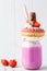 Pink strawberry freakshake cocktail with donut and sweets, white background. Unhealthy desserts concept