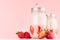 Pink strawberry smoothies with piece juicy fruits in retro jars with red striped straws on light soft pastel pink wall.