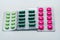 Pink tablets and green capsule and green tablets in blister pack on white background. Painkiller medicine. Pharmaceutical industry