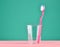 Pink toothbrush in a transparent cup on a minty green pastel background, minimalist trend.