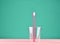 Pink toothbrush in a transparent cup on a minty green pastel background, minimalist trend.