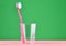 Pink toothbrush in a transparent cup on a minty green pastel background, minimalist trend.
