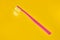 Pink toothbrush on yellow background for oral hygiene to clean teeth, gums and tongue