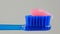 Pink toothpaste is placed on a blue toothbrush on a white background close-up.
