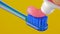 Pink toothpaste is placed on a blue toothbrush on a yellow background close-up.