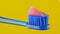 Pink toothpaste is placed on a blue toothbrush on a yellow background close-up.