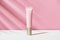 Pink tube of soft organic natural eye cream with golden cap on white pink background, palm leaf shadow. Summer facial product, sun