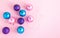 Pink, turquoise and purple satin Christmas balls on a pink background with small lights around them. Christmas decoration for