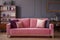 Pink velvet couch with decorative pillows standing in grey living room interior with vintage cupboard, fresh plants and molding o