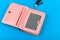 Pink wallet on a blue background. Wallet with a black tassel. A place to write. Close-up. Pink leather wallet isolated on a blue