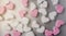 Pink and white heart-shaped marshmallows evenly laid out on gray aluminum background