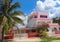 Pink and white Mexican three story house with red fence and palm and flowering trees against a beautiful blue sky with fluffy clou