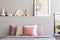 Pink and white pillows on grey bed in pastel bedroom interior with poster on bedhead. Real photo