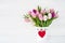 Pink and white tulips bouquet in white vase decorated with red heart. Valentines Day concept.