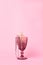 Pink wine glass on a pastel pink background. Beads and a gift box are in the glass. All objects and background are in pink color.