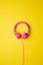 pink wired headphones centered on a flat yellow background