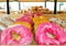 Pink and yellow choux donuts, various baked goods and puff pastry serving for sell on a shelfs in supermarket bakery
