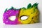 Pink and yellow feather carnival domino mask with green feather outline and golden jewellry decorations