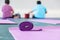 The pink yoga mat has a purple rope on top. The carpet is laid on the green concrete floor. There are elderly women sitting in the