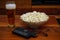 Pint of beer bowl of popcorn remote controllers and glasses on wooden background homemade entertainment