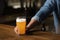 Pint of beer in trendy bar. Bartender puts glass of light beer with foam on table